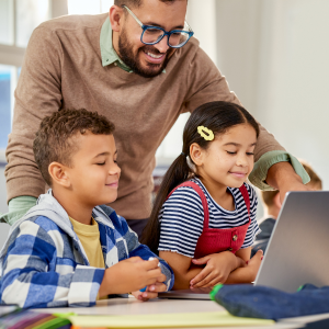 two young students and teacher looking at an open laptop